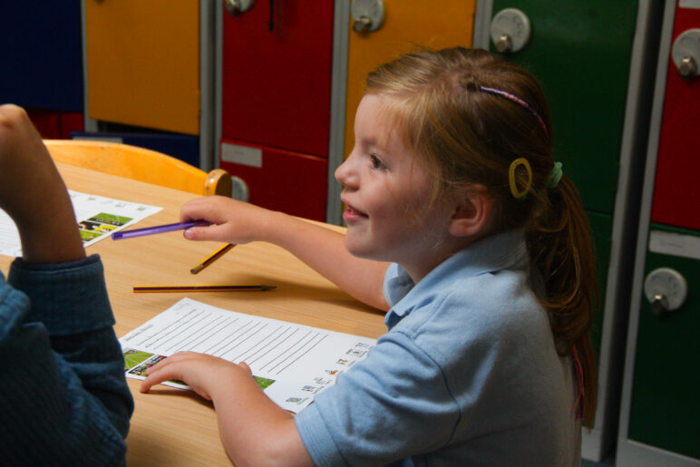 A young child sitting at a table completing an activity sheet.