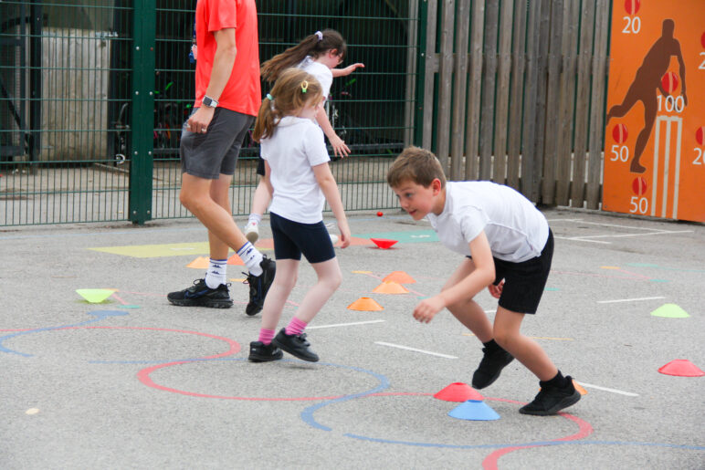 A group of children playing a physical, active game during a PE lesson on the school playground.
